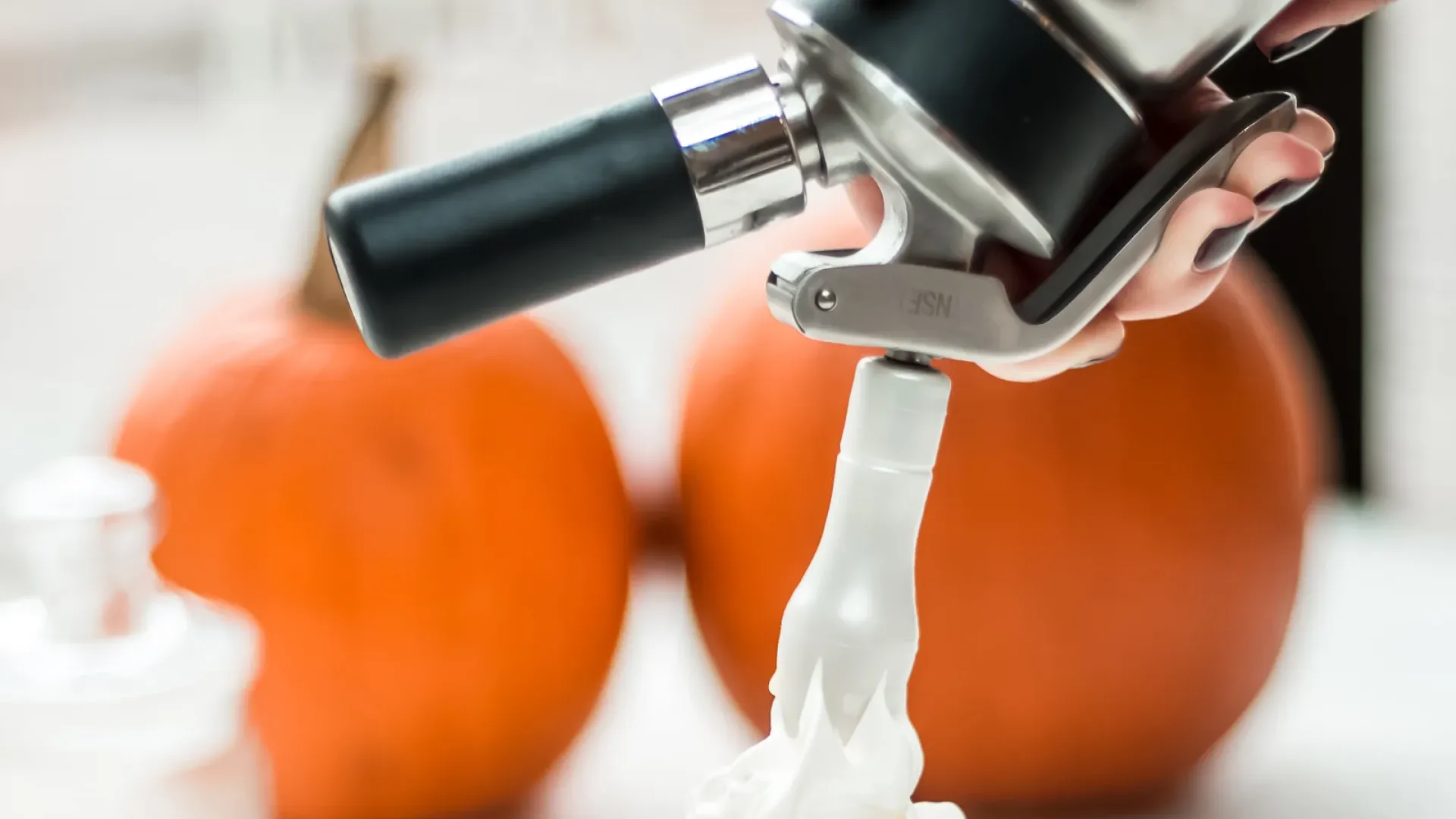 Close-up of a whipped cream dispenser head showing stainless threads, gasket, and valve assembly