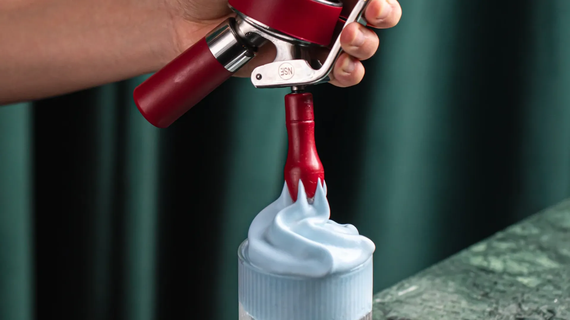 Stainless steel whipped cream dispensers lined up for comparison testing in a commercial kitchen